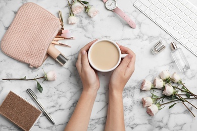 Photo of Woman holding cup of coffee on marble table with roses and keyboard, top view