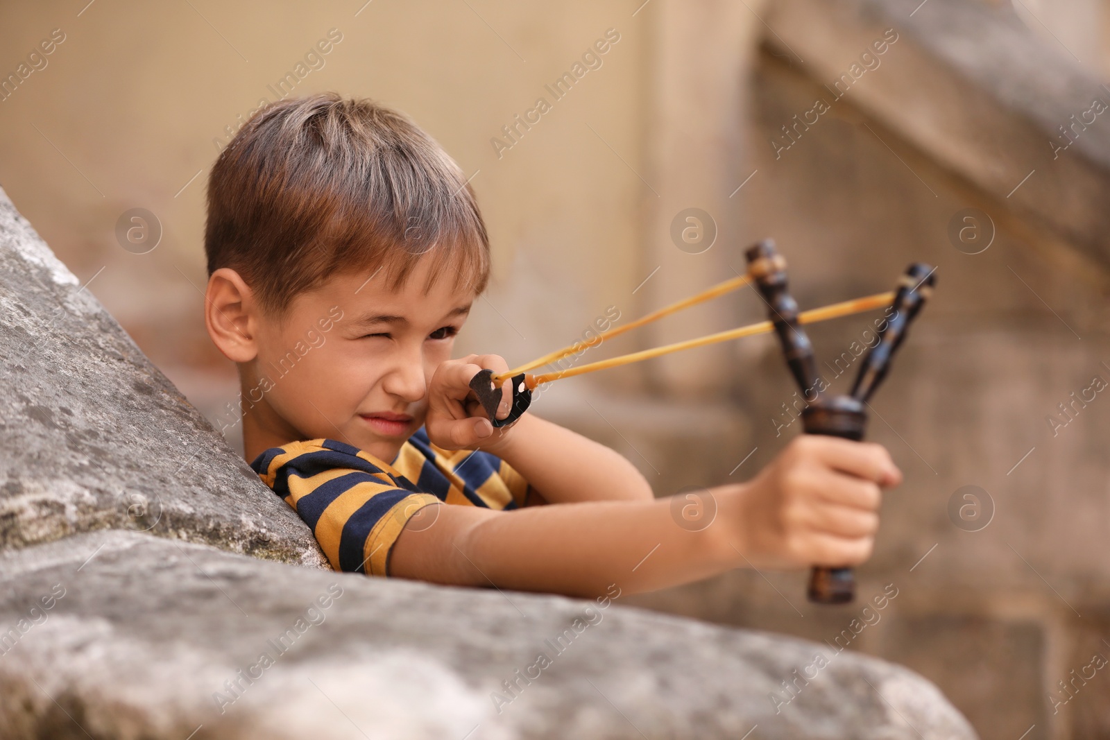 Photo of Cute little boy playing with slingshot outdoors