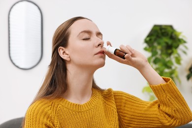 Photo of Medical drops. Young woman using nasal spray indoors