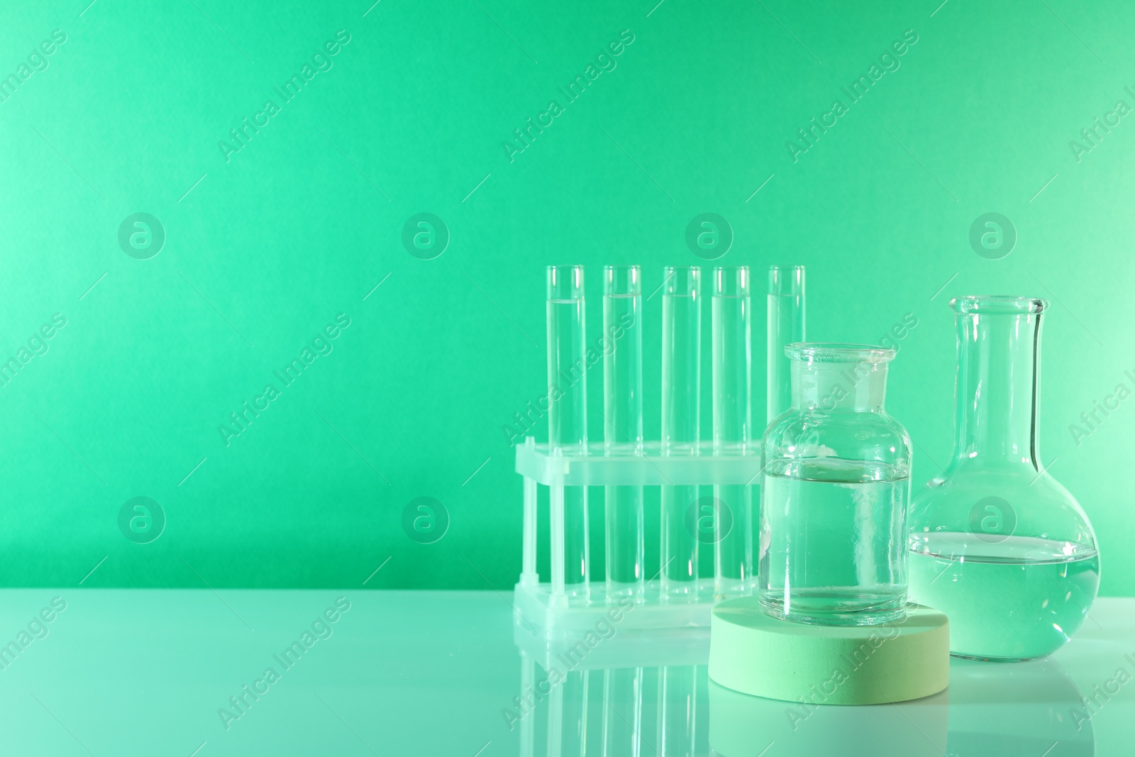 Photo of Laboratory analysis. Different glassware on table against green background, space for text