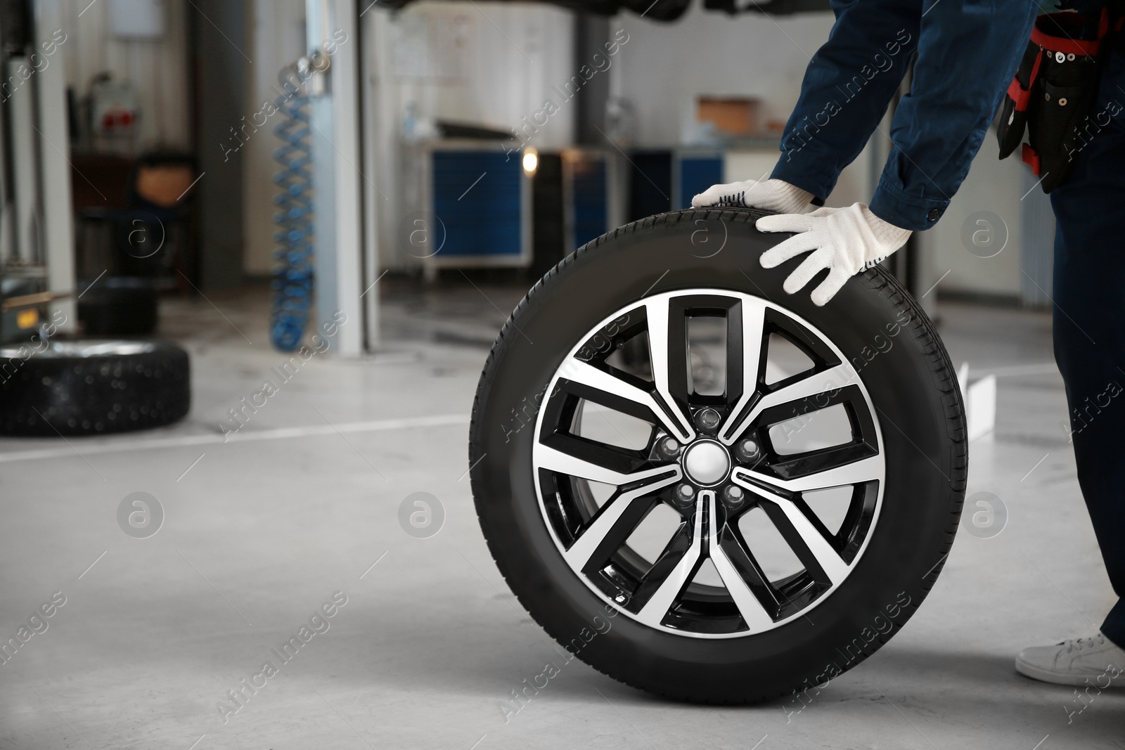 Photo of Technician rolling car wheel in automobile repair shop closeup. Space for text
