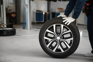 Technician rolling car wheel in automobile repair shop closeup. Space for text