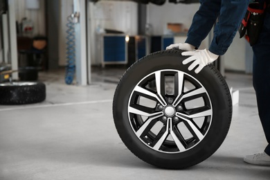 Photo of Technician rolling car wheel in automobile repair shop closeup. Space for text