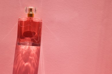 Photo of Luxury women's perfume. Sunlit glass bottle on pink background, top view. Space for text