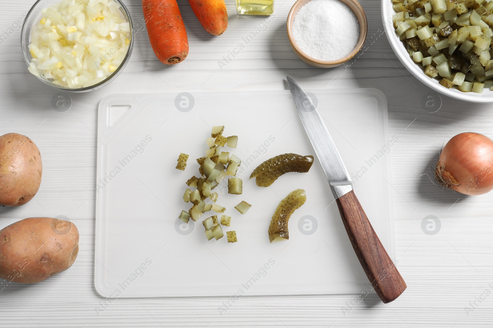 Photo of Cut pickled cucumbers near ingredients on white wooden table, flat lay. Cooking vinaigrette salad