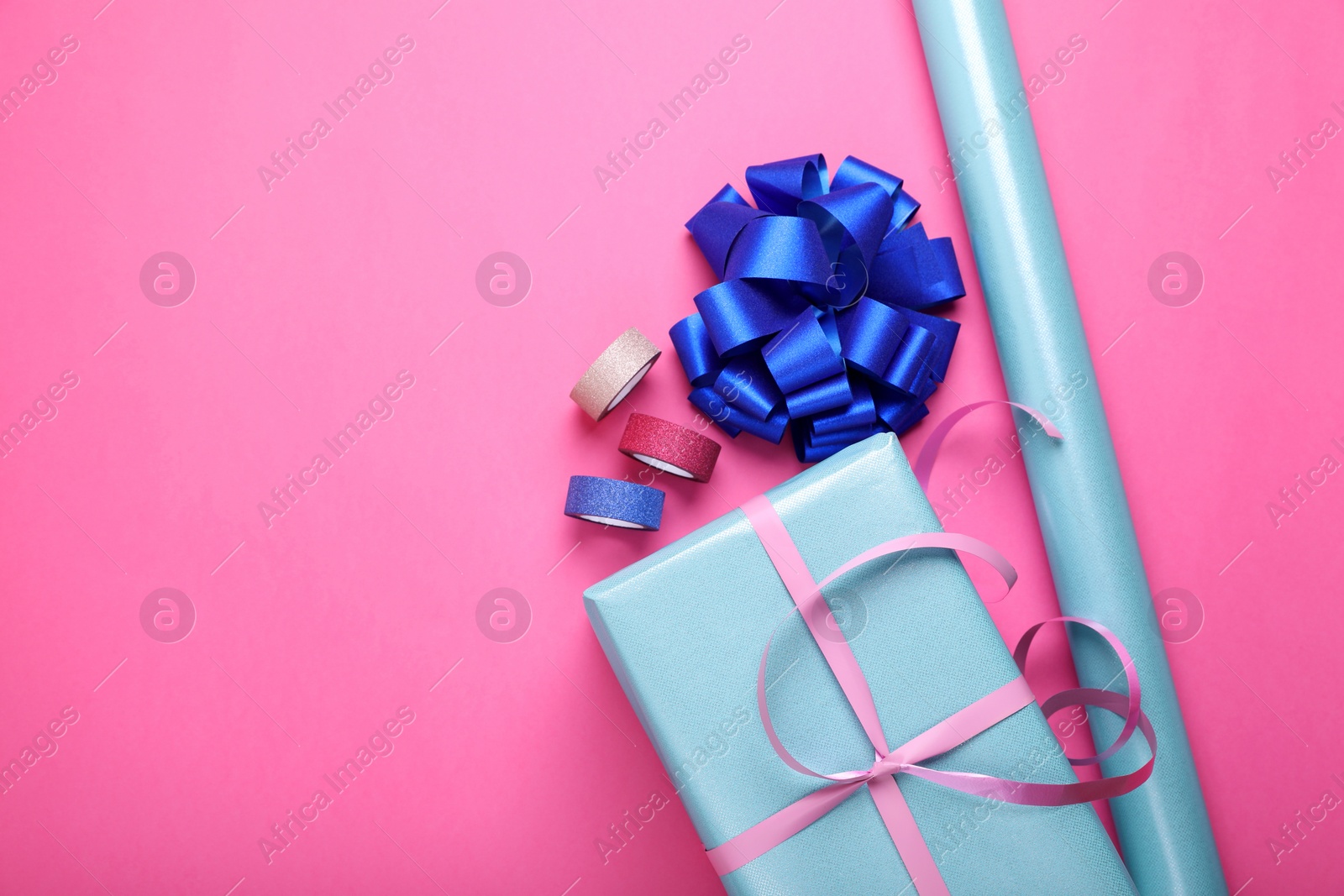 Photo of Roll of wrapping paper, gift box, bow and ribbons on pink background, flat lay. Space for text