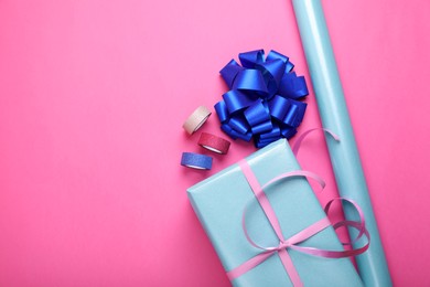 Photo of Roll of wrapping paper, gift box, bow and ribbons on pink background, flat lay. Space for text