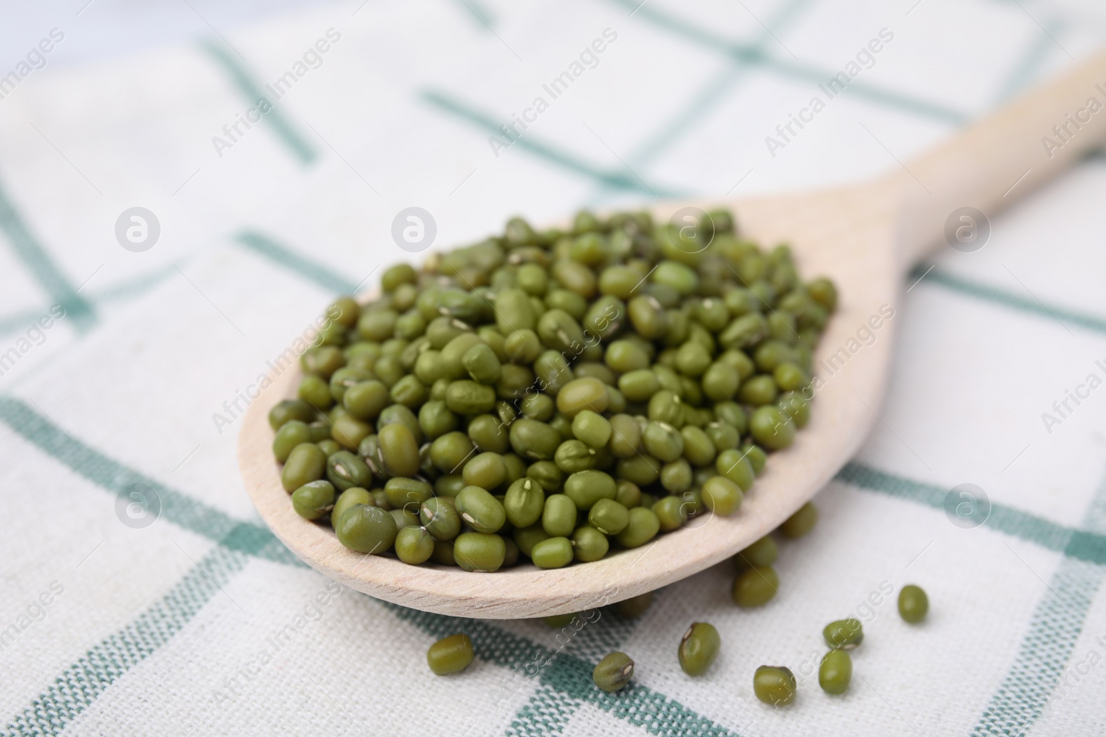 Photo of Wooden spoon with mung beans on kitchen towel, closeup