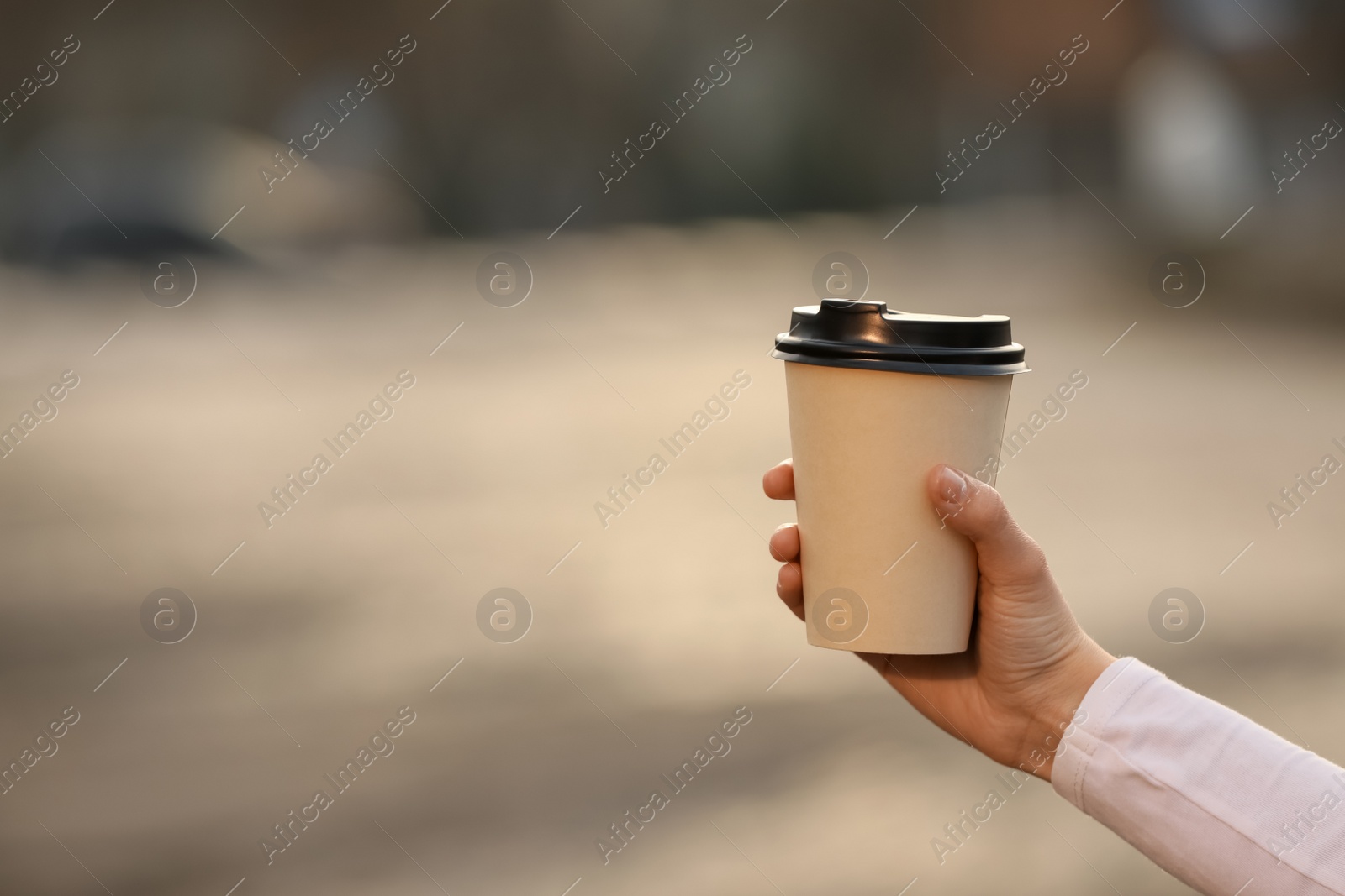 Photo of Woman holding paper coffee cup outdoors, closeup. Space for text