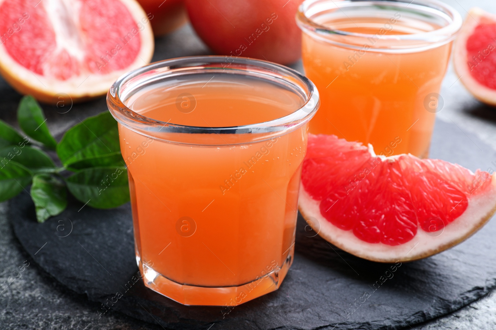 Photo of Tasty freshly made grapefruit juice and fruit on grey table