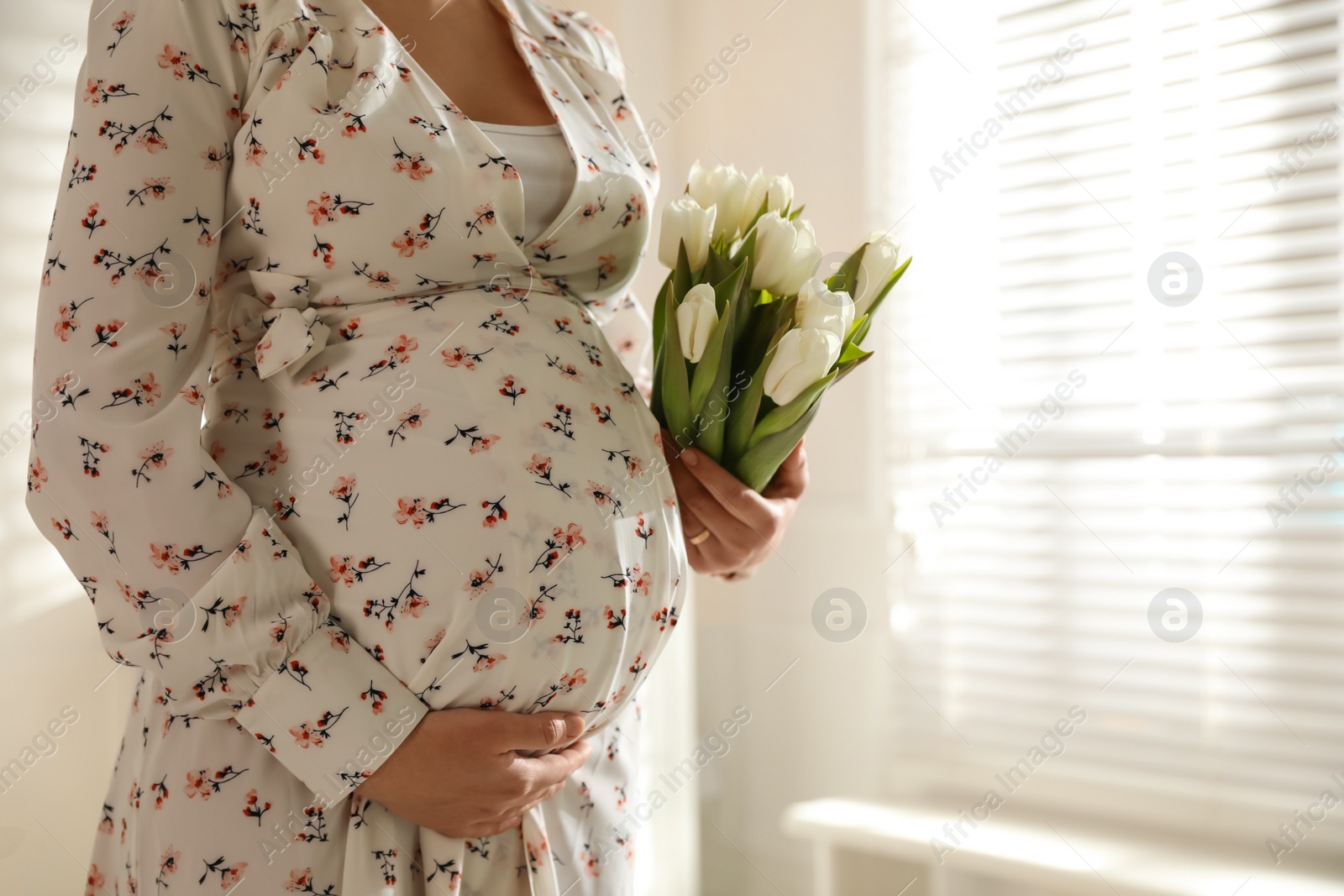 Photo of Young pregnant woman with flowers indoors, closeup