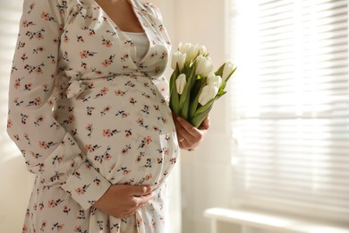 Young pregnant woman with flowers indoors, closeup