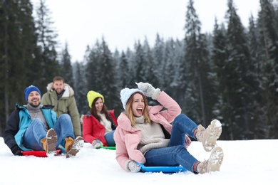 Happy friends sliding on sleds outdoors. Winter vacation