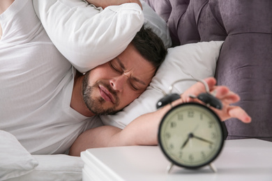 Photo of Sleepy man turning off alarm clock at home in morning