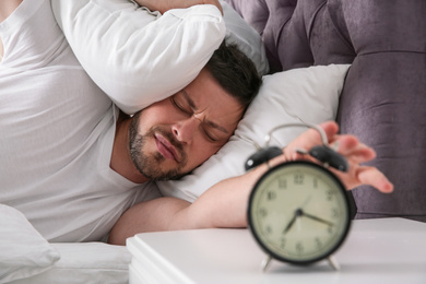 Sleepy man turning off alarm clock at home in morning