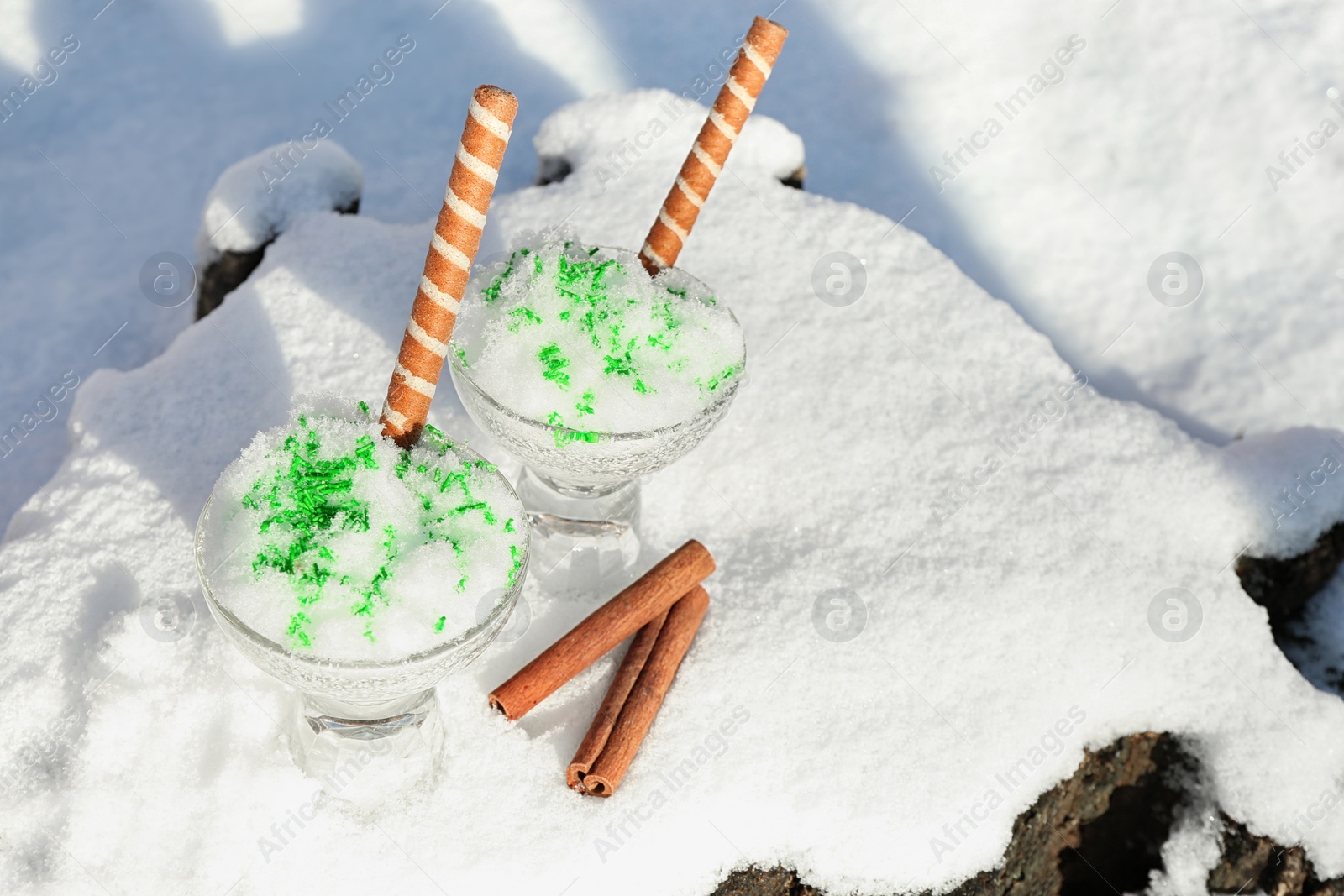 Photo of Glass bowls with tasty ice cream and waffle rolls on snow