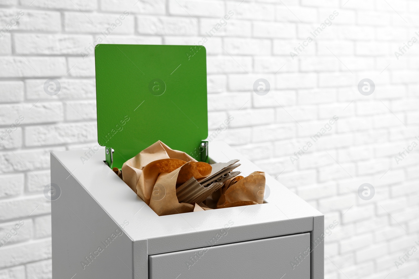 Photo of Trash bin with paper and cardboard near brick wall, space for text. Recycling concept