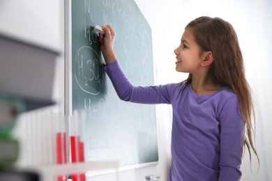 Schoolgirl writing chemical formulas on chalkboard in classroom