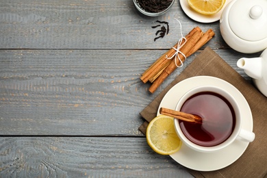 Photo of Delicious hot tea with cinnamon and lemon on grey wooden table, flat lay. Space for text