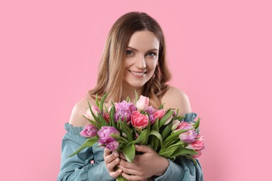 Happy young woman with bouquet of beautiful tulips on pink background