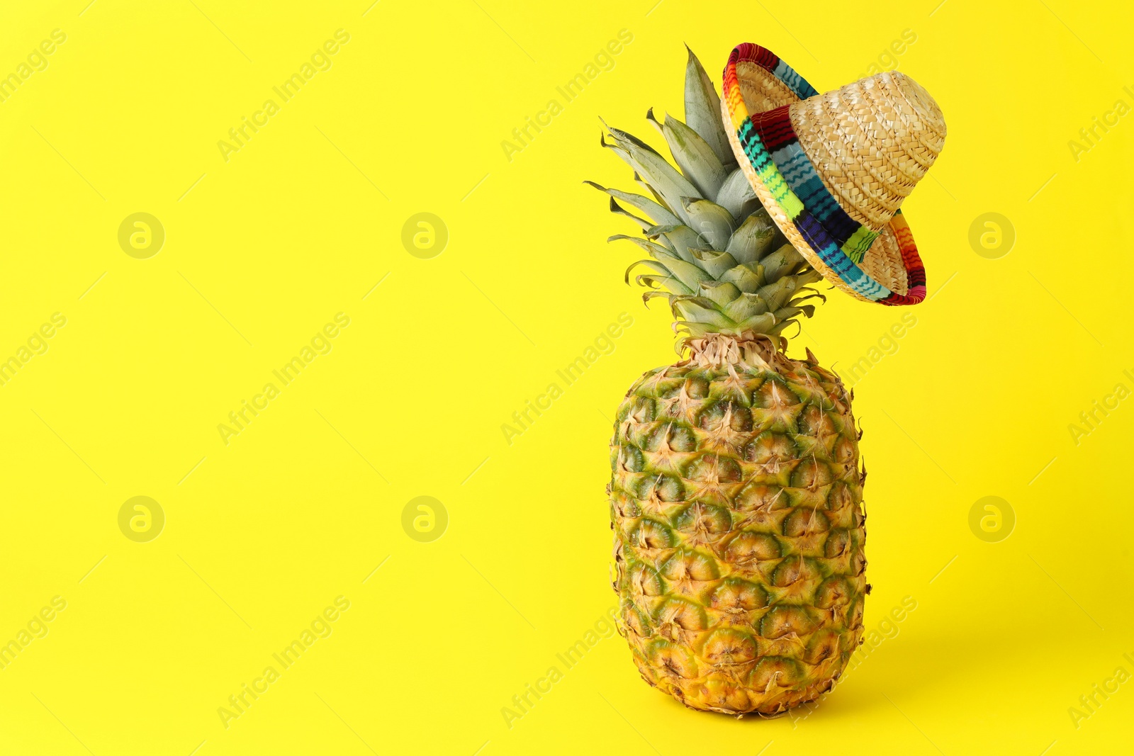 Photo of Pineapple with Mexican sombrero hat on yellow background, space for text