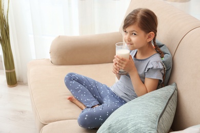 Photo of Cute little girl drinking milk on sofa at home