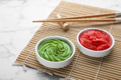 Swirl of wasabi paste, pickled ginger, chopsticks and bamboo mat on white marble table