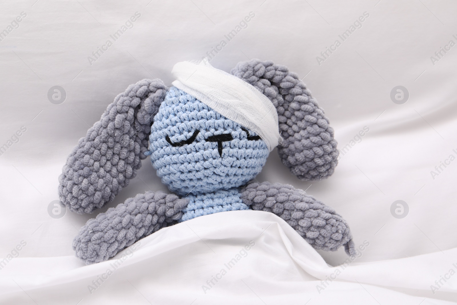 Photo of Toy cute bunny with bandage under blanket in bed