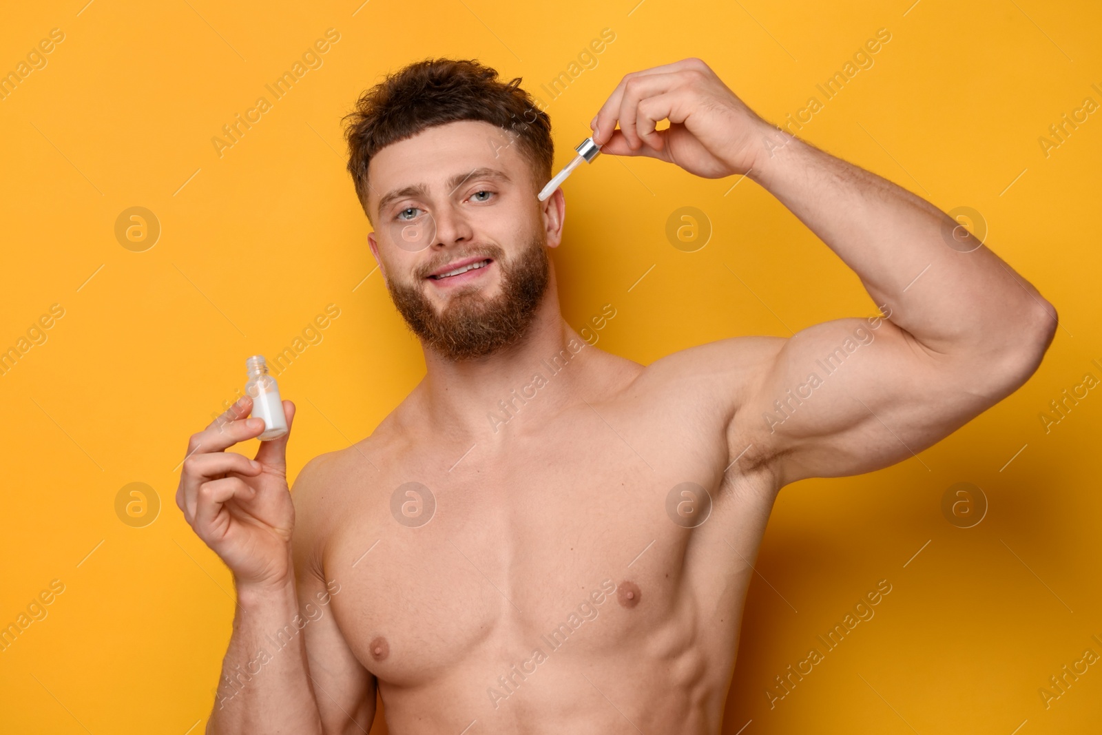 Photo of Handsome man applying serum onto his face on orange background