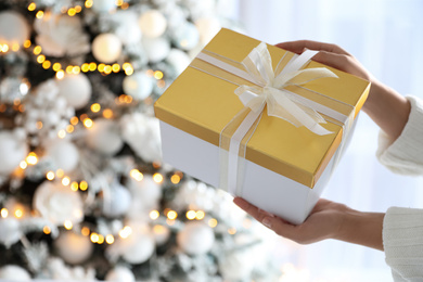 Woman holding gift box near Christmas tree. Festive interior