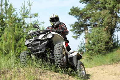 Photo of Man driving modern quad bike on sandy road near forest. Extreme sport