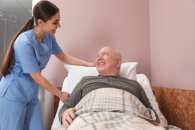 Nurse assisting senior man on bed in hospital ward