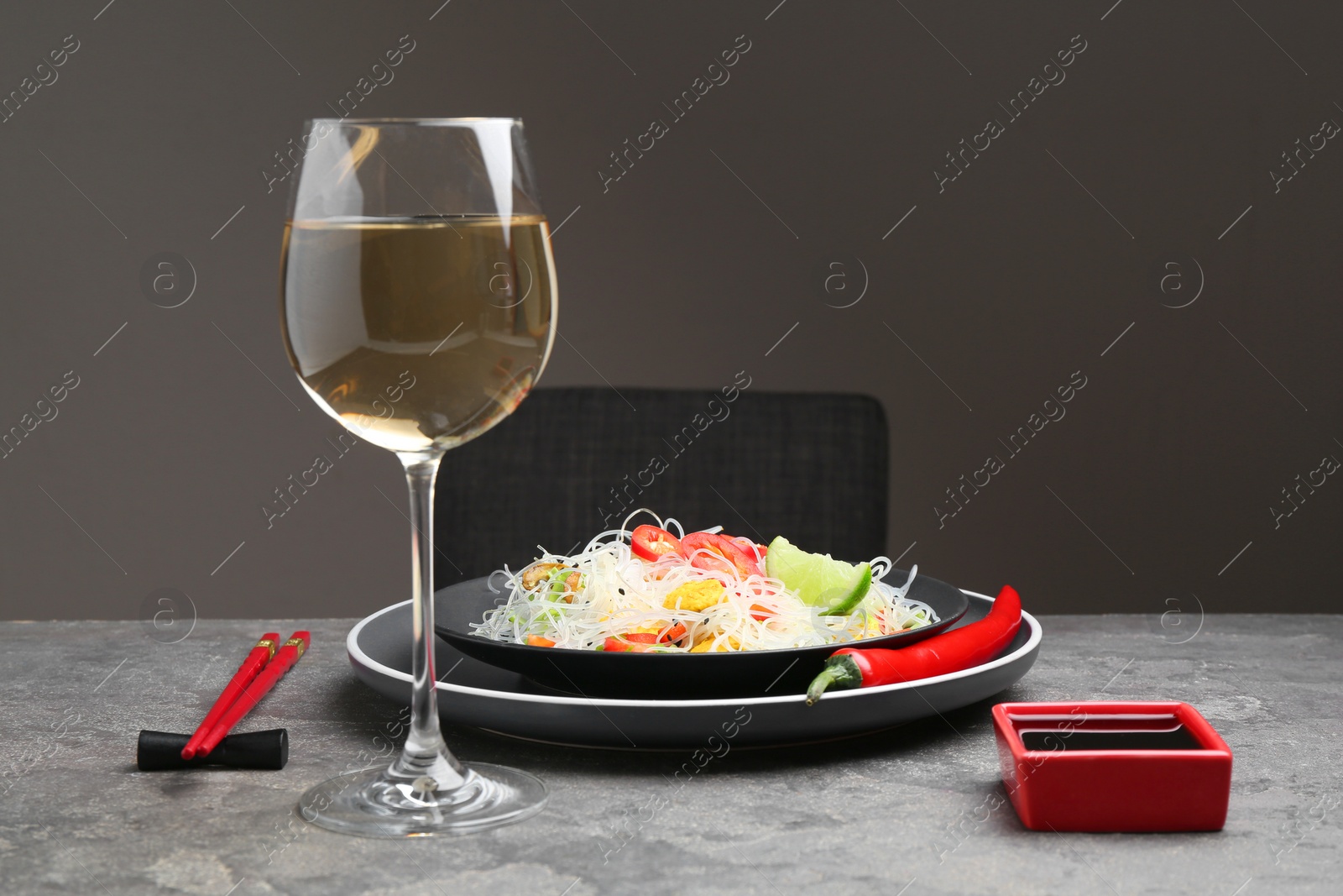 Photo of Stir-fry. Tasty rice noodles with meat and vegetables served on grey textured table