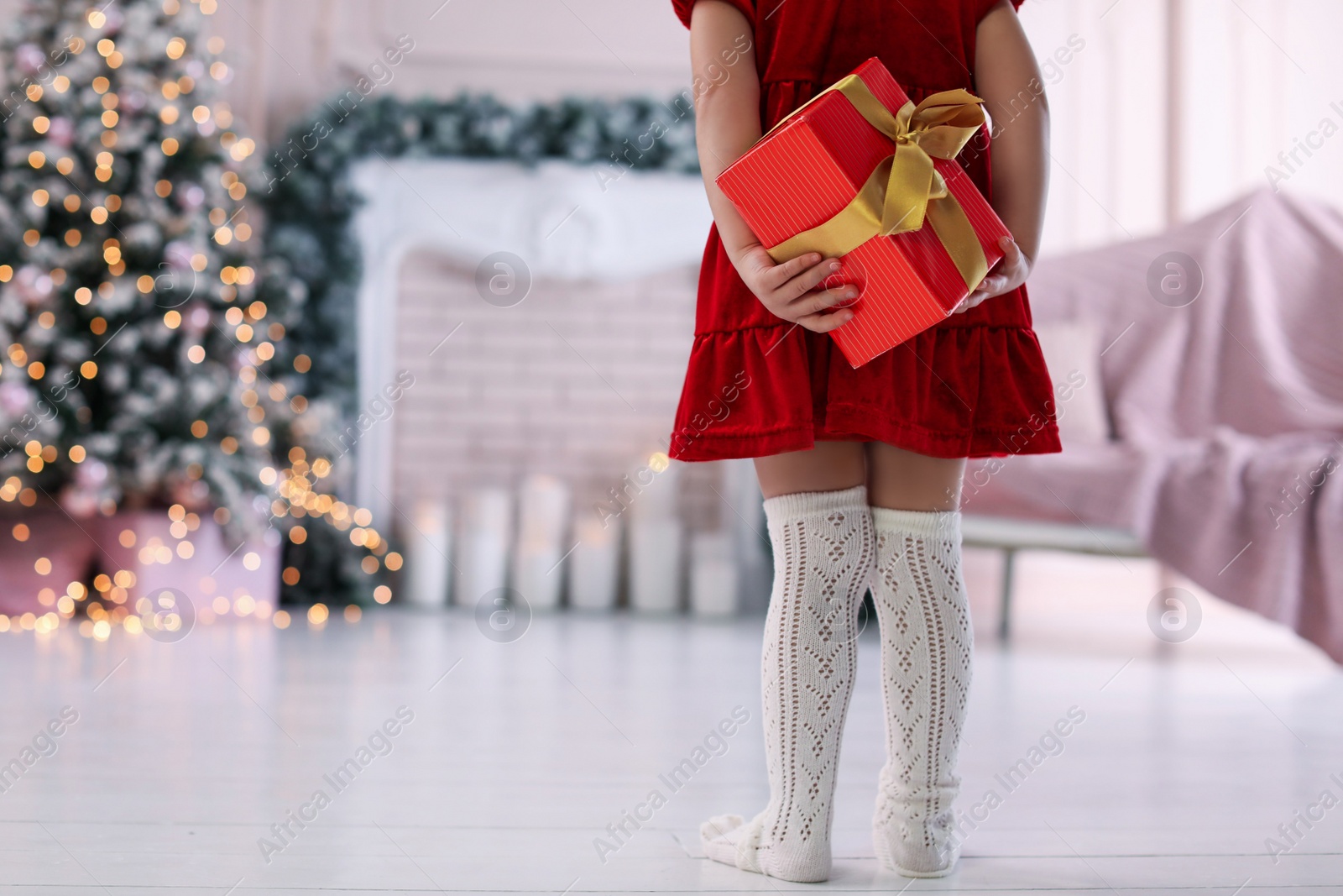 Photo of Cute little child hiding Christmas gift behind her back at home. Space for text