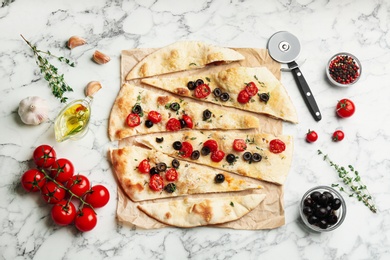 Delicious focaccia bread with olives and tomatoes on white marble table, flat lay