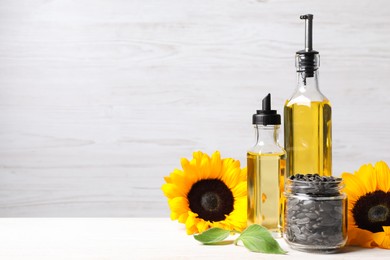 Photo of Bottles of sunflower cooking oil, seeds and yellow flowers on white wooden table, space for text