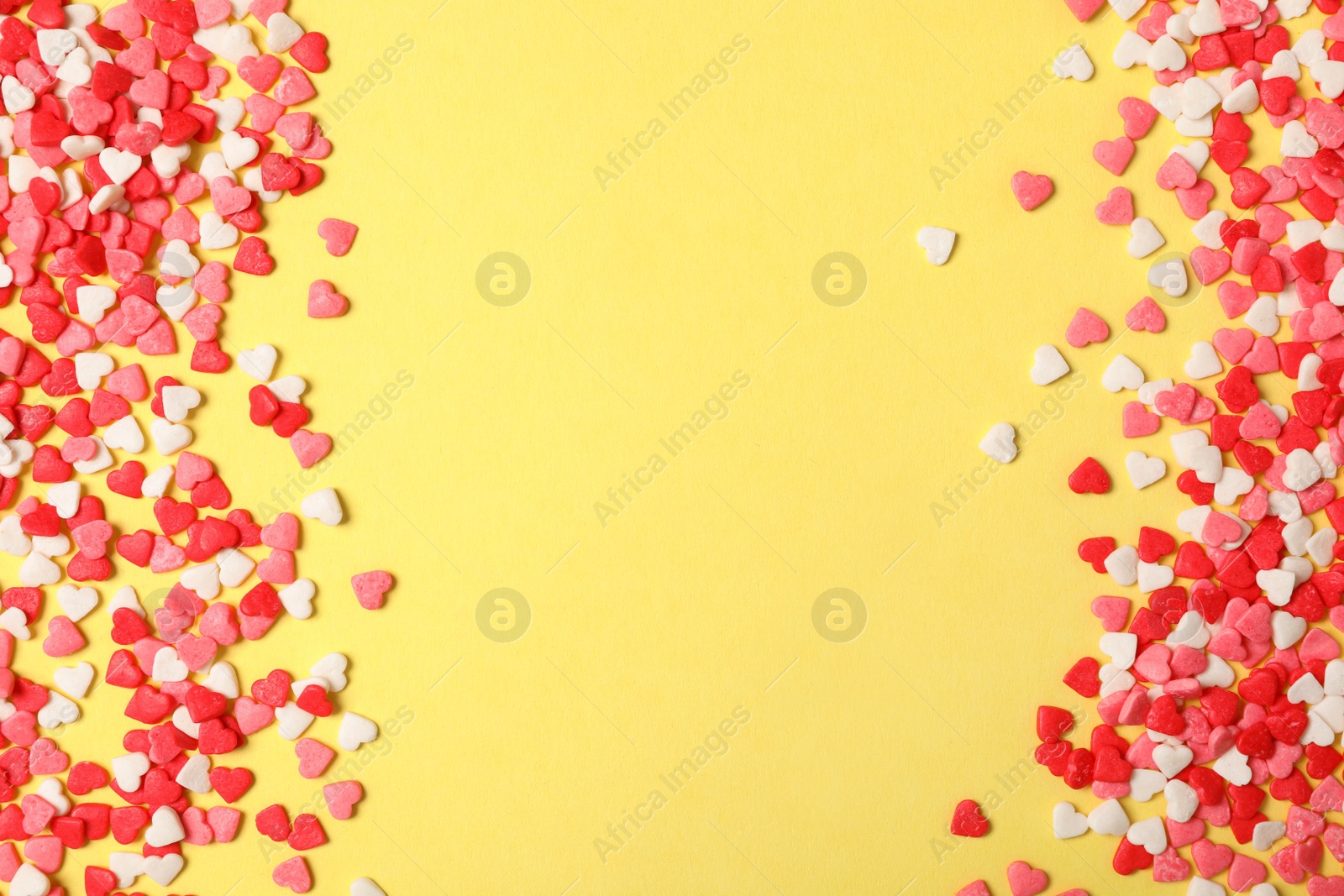 Photo of Bright heart shaped sprinkles on yellow background, flat lay. Space for text