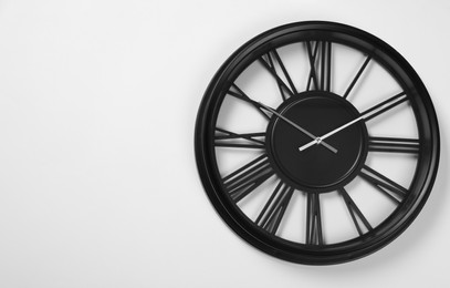 Stylish analog clock hanging on white wall, space for text