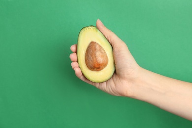 Woman holding ripe cut avocado on color background