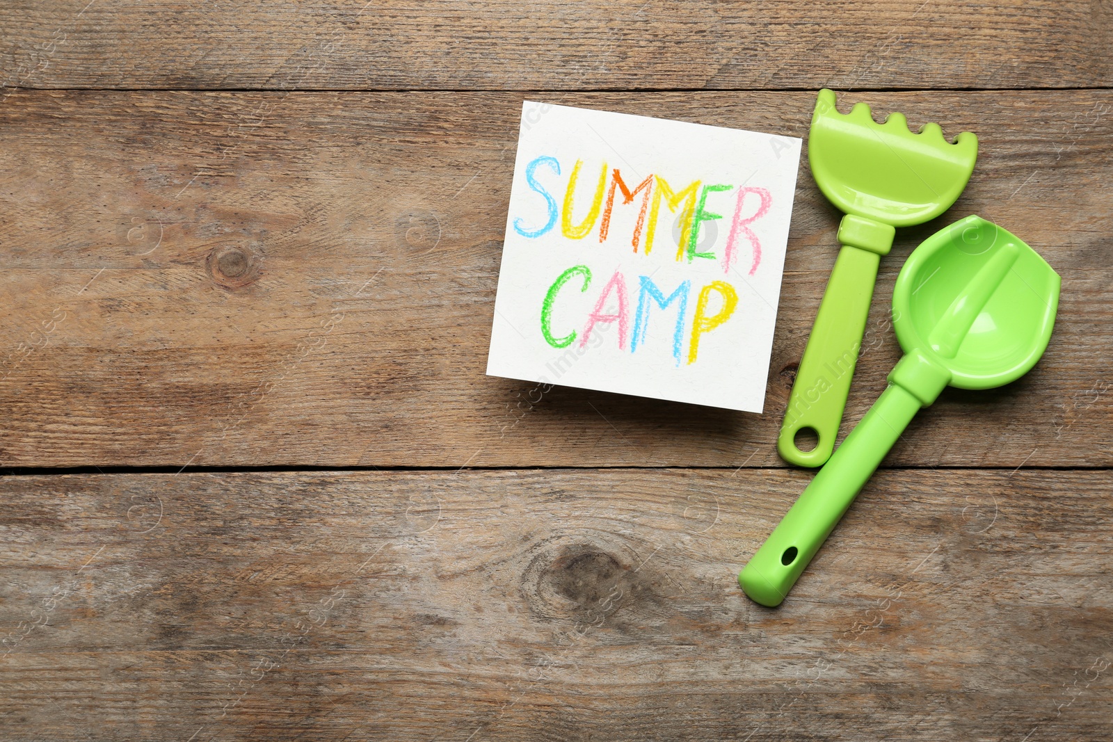 Photo of Card with text SUMMER CAMP and beach toys on wooden table, flat lay. Space for design