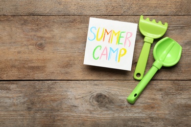 Card with text SUMMER CAMP and beach toys on wooden table, flat lay. Space for design