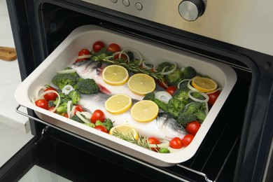 Photo of Raw fish with vegetables and lemon in baking dish into oven indoors