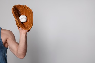 Photo of Athletic man with glove and baseball ball on light grey background, closeup. Space for text