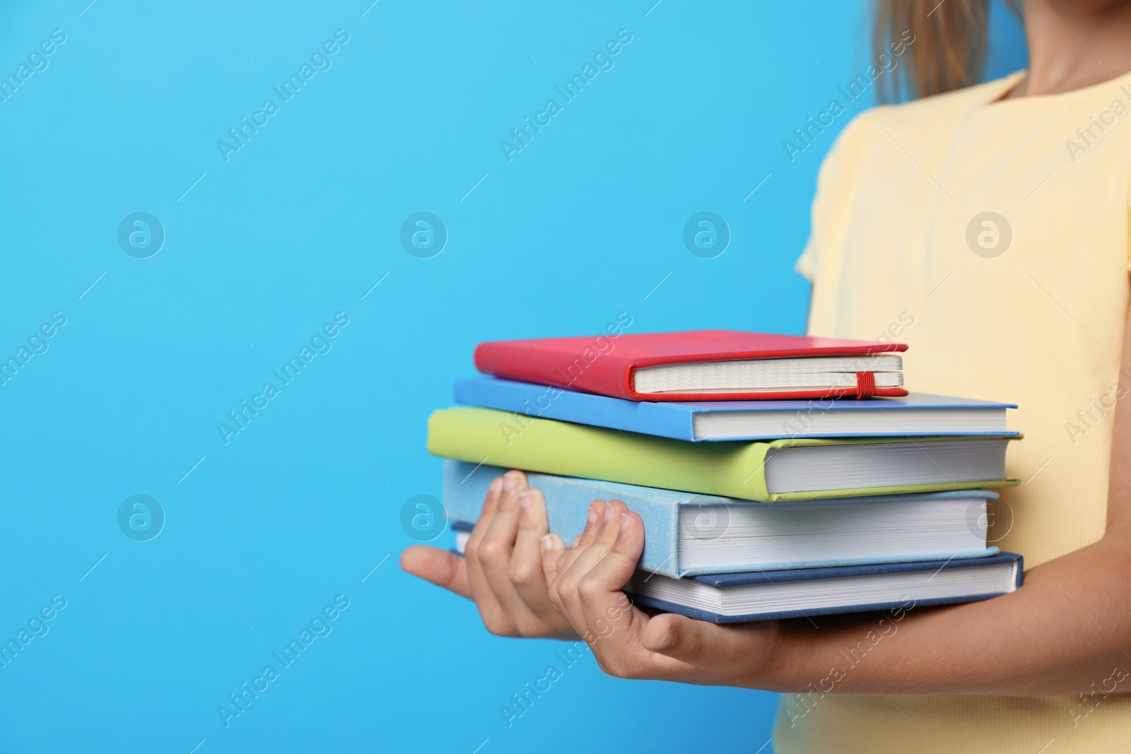 Photo of Little girl holding books on blue background, closeup. Reading concept