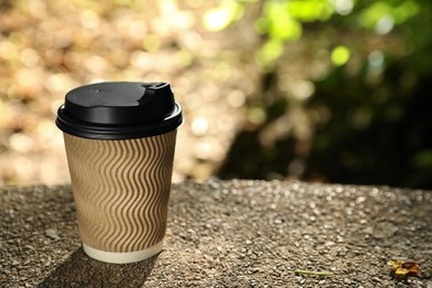 Cardboard takeaway coffee cup with plastic lid on stone parapet outdoors, space for text