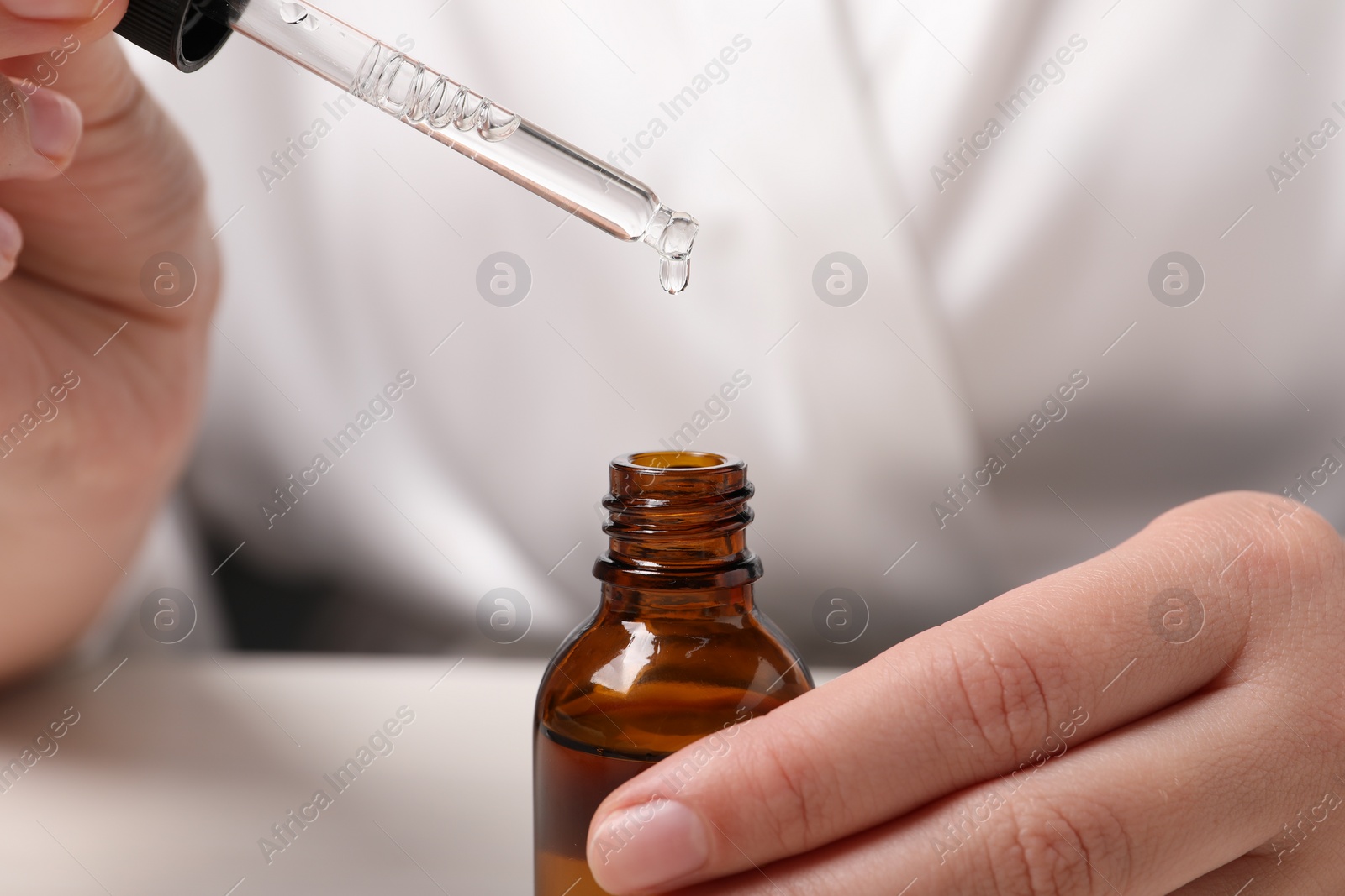 Photo of Woman with bottle of cosmetic serum and pipette at white table, closeup