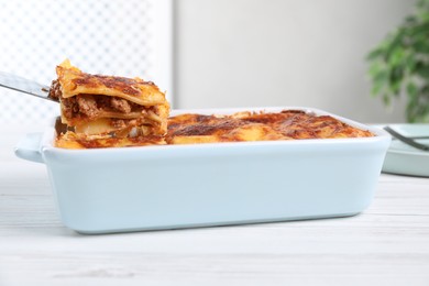 Tasty cooked lasagna in baking dish on white wooden table