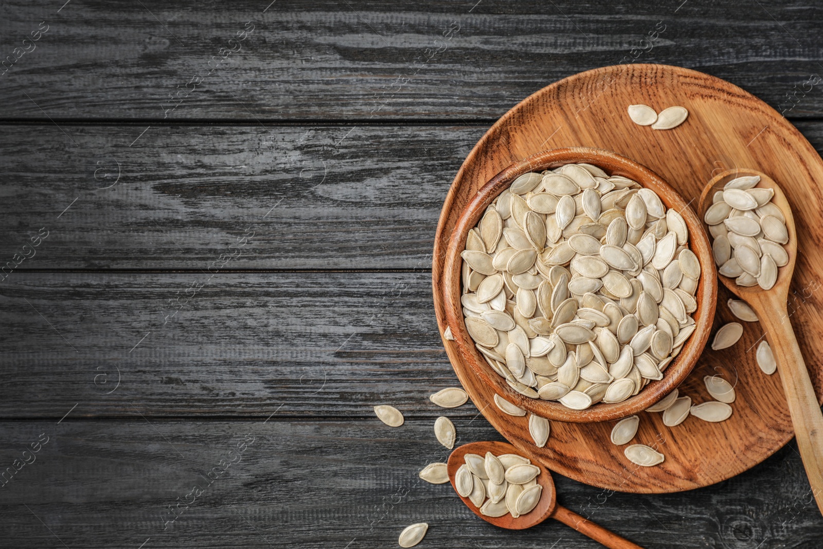 Photo of Raw pumpkin seeds in dish on wooden background, top view. Space for text