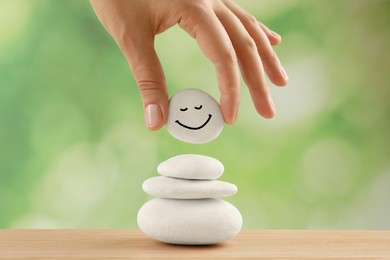 Photo of Woman putting stone with drawn happy face on stack, closeup Zen concept