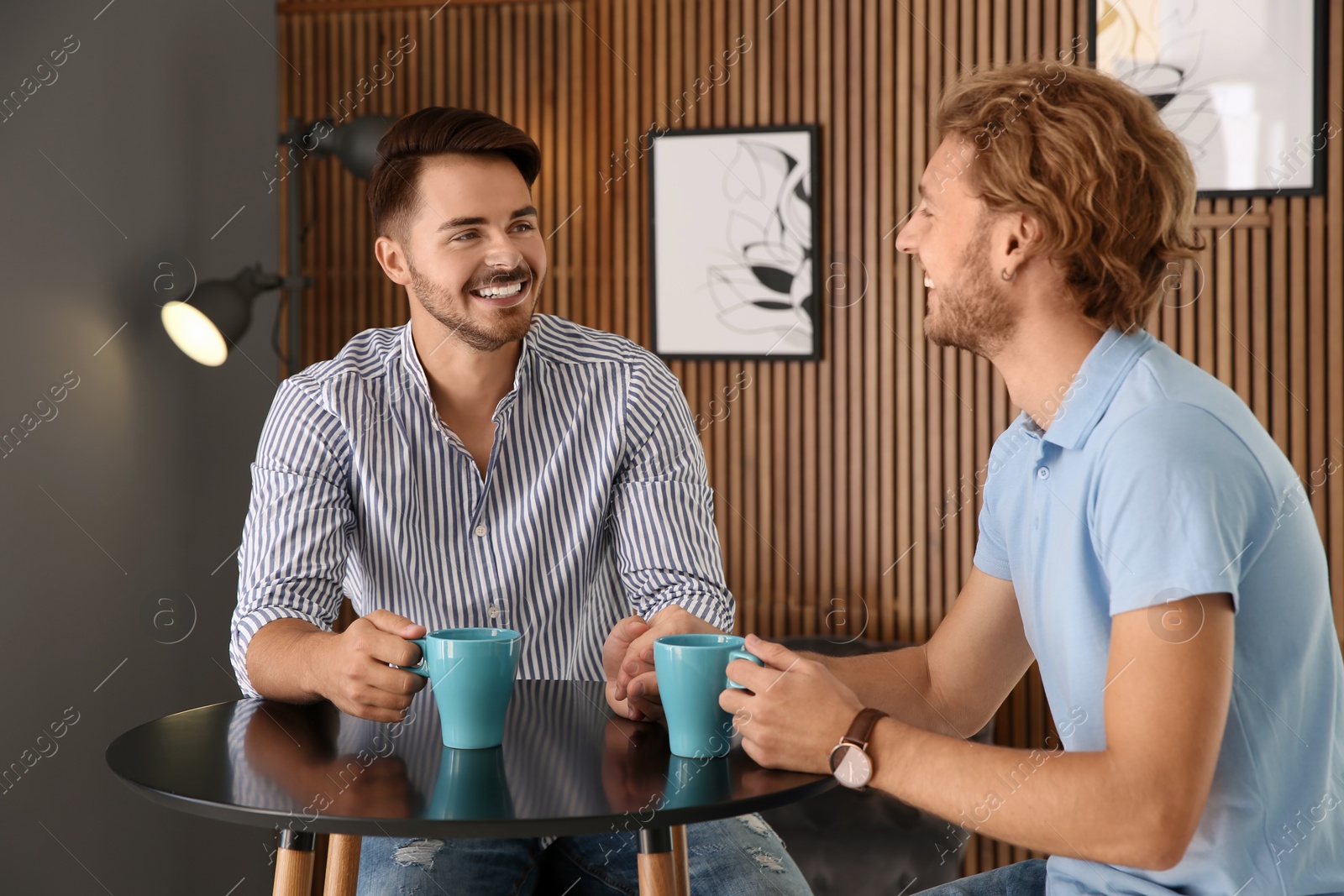 Photo of Happy gay couple with coffee at table indoors